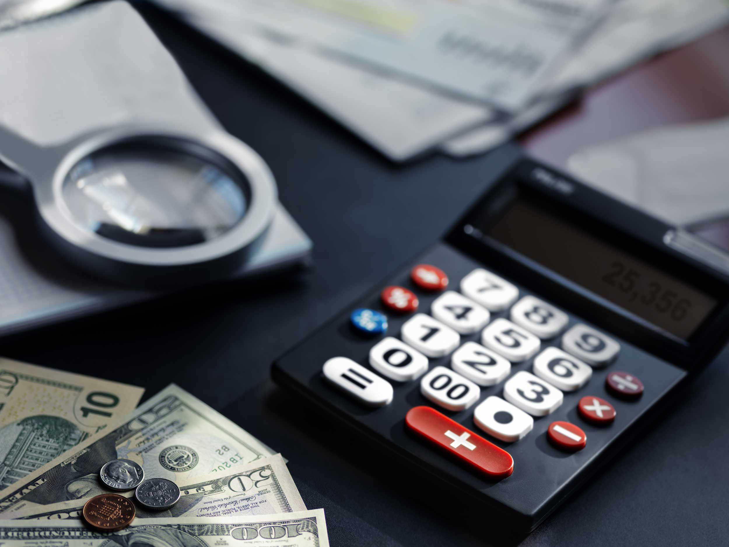 An accountant's desk with money, magnifying glass, and a calculator on it