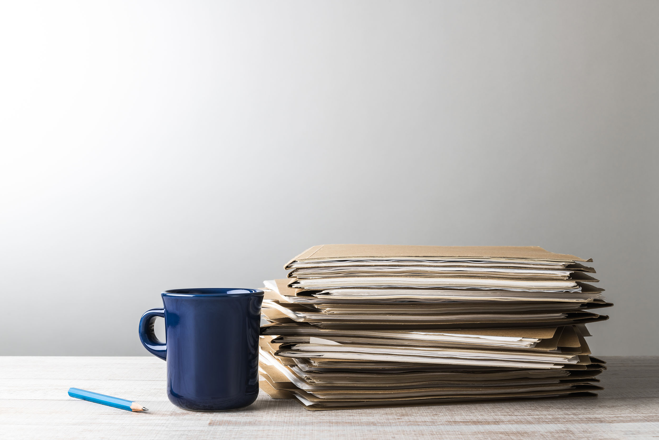 A bookkeeper's desk displaying a small stack of folders, a coffee mug, and a pencil