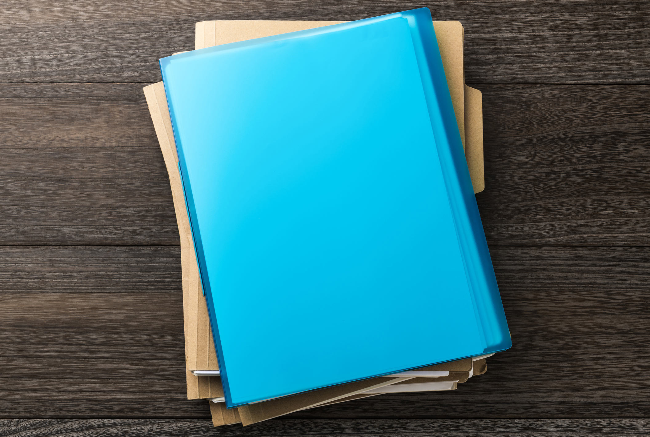 A flatlay desk displaying folders stacked on top of each other with a blue folder on top