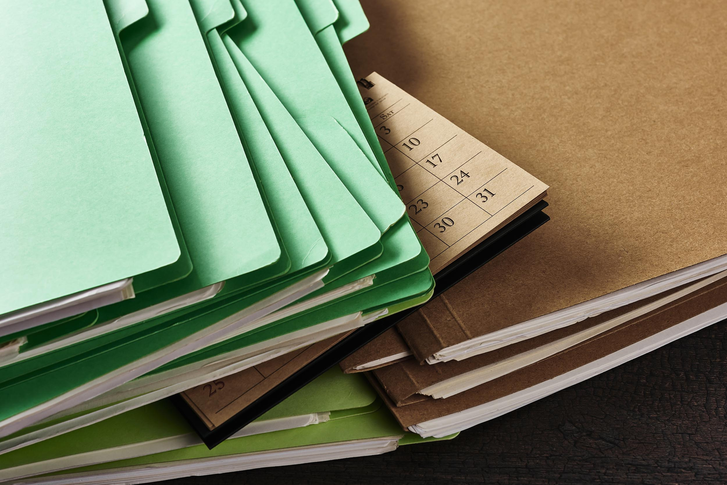 A pile of brown and green folder, as well as a calendar, on a bookkeeper's desk