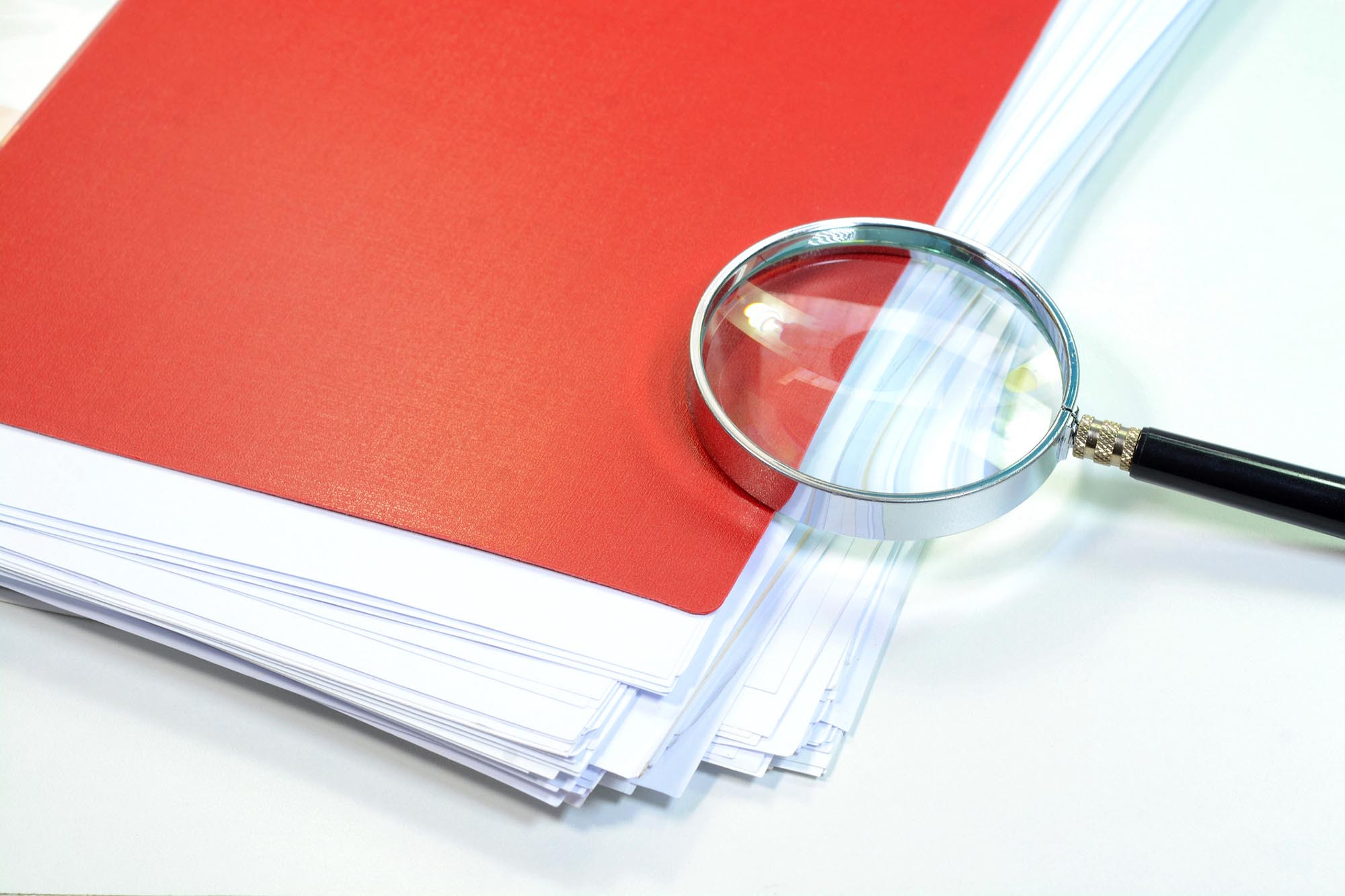 A red folder and magnifying glass on a desk