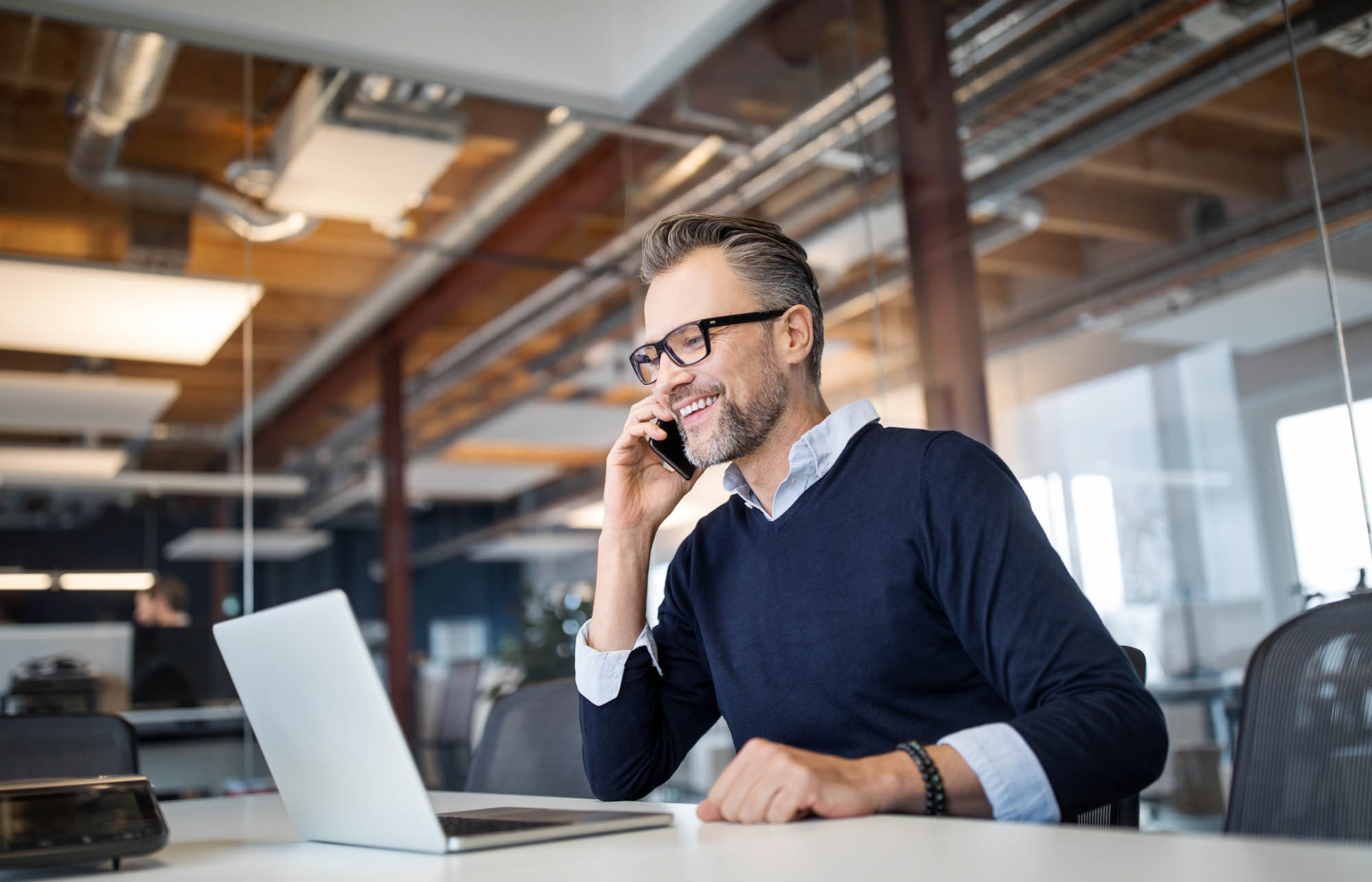 Man in a business casual office setting calls a client while looking at his computer.