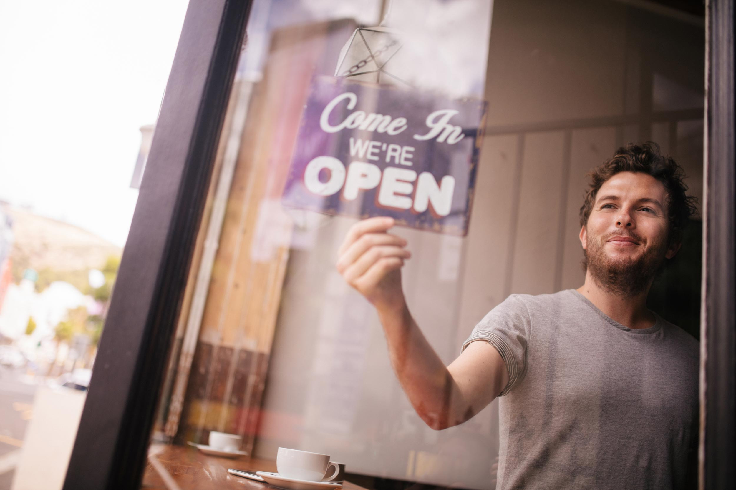 Cafe owner flips his 'Come In We're Open" sign to open.