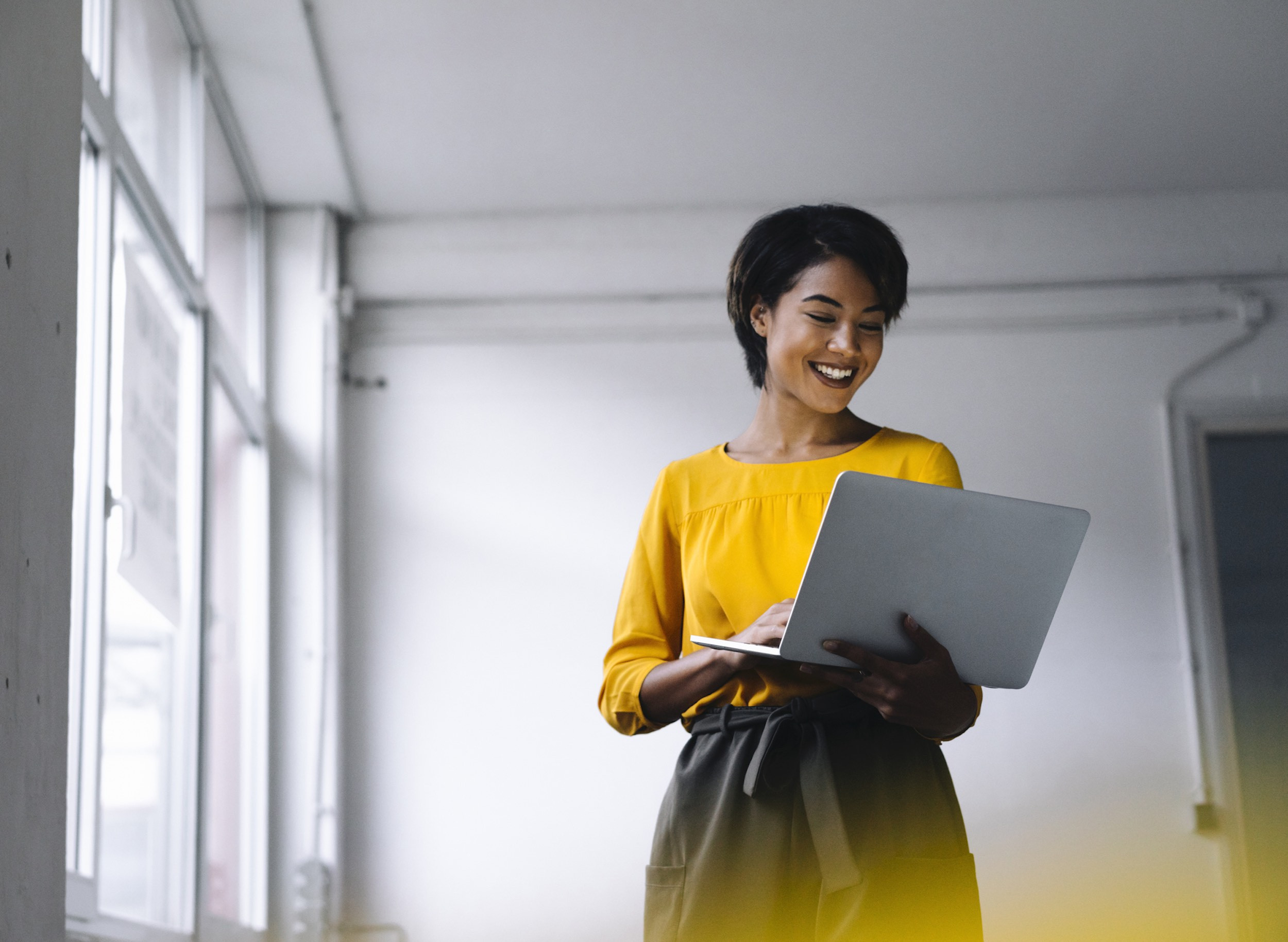 Smiling entrepreneur works on her laptop while standing up.