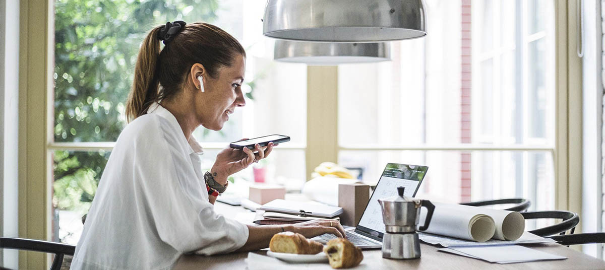 Business professional using voice commands on a smartphone while working on a laptop