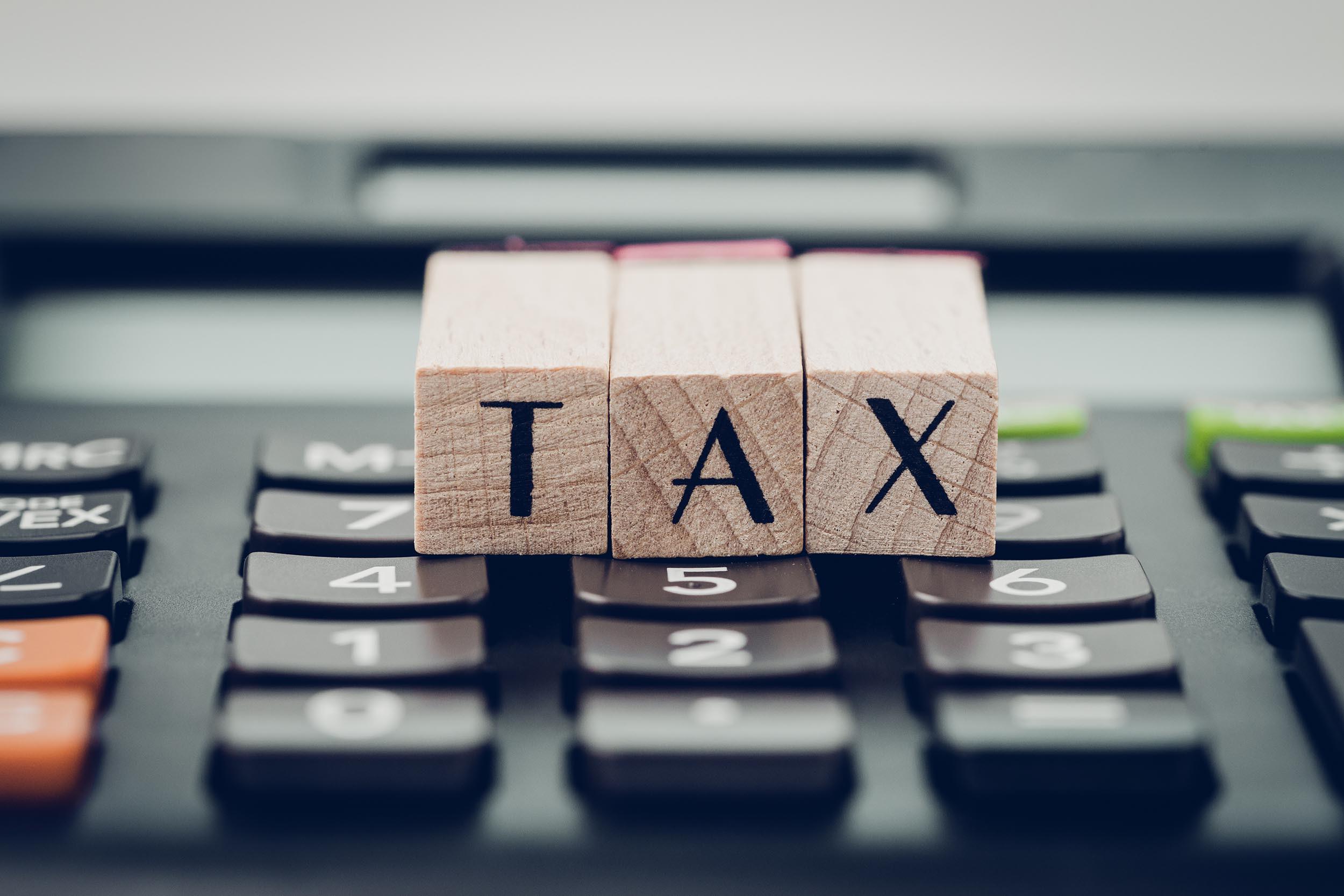 Tax calculation or submission concept, small wooden stamp with alphabet combine the word TAX on black calculator