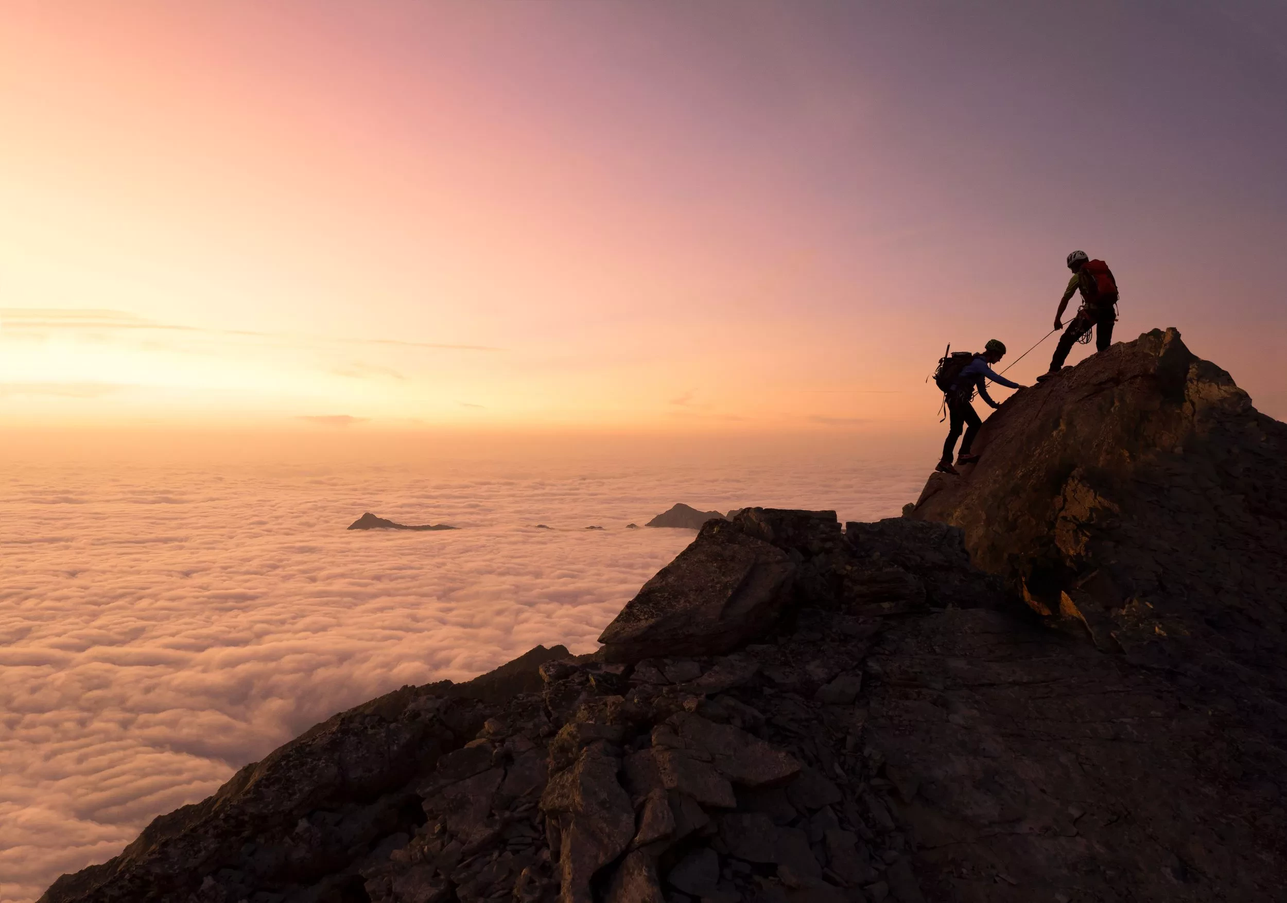 two people helping each other climb a mountain