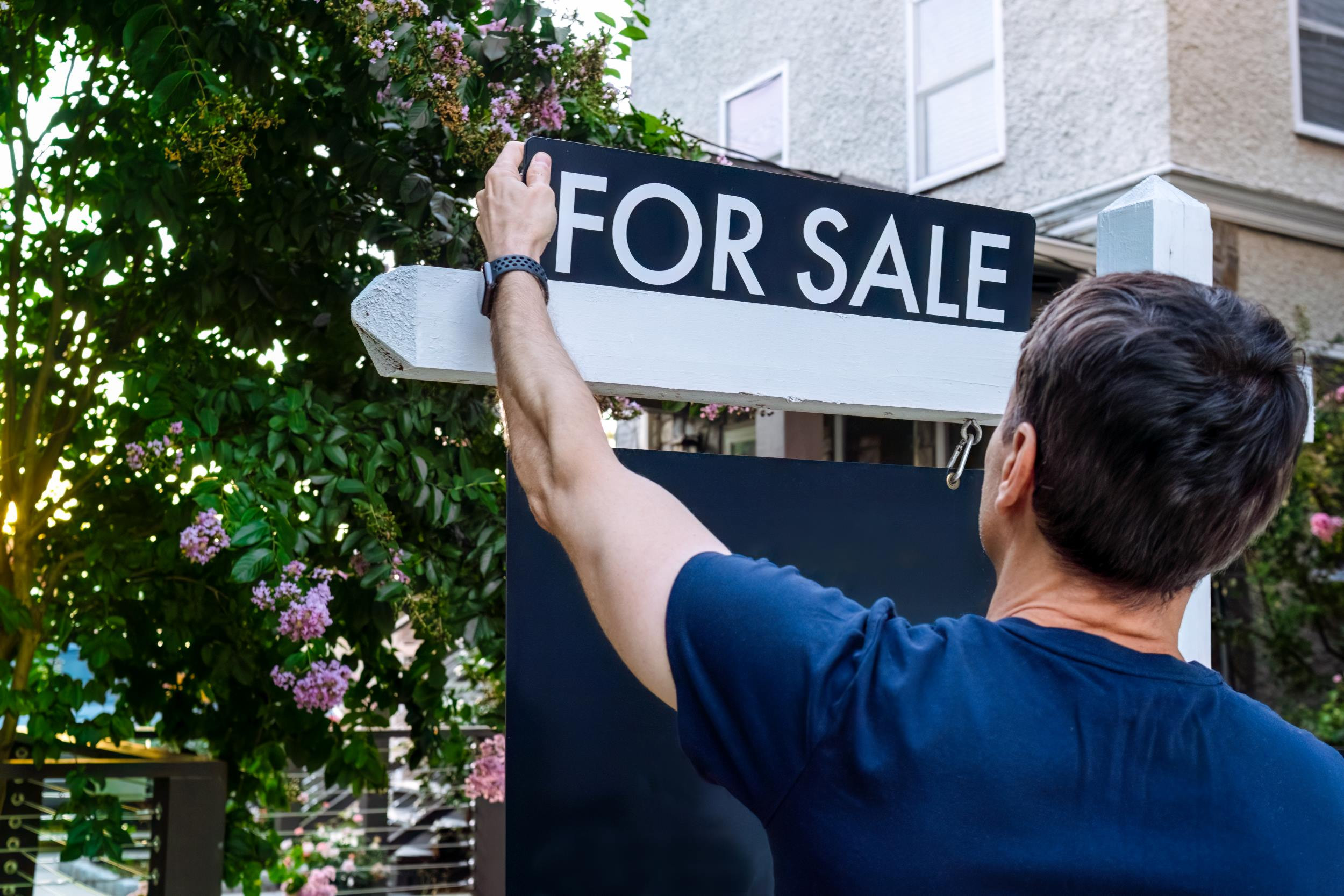 a man putting up a For Sale sign in front of his house