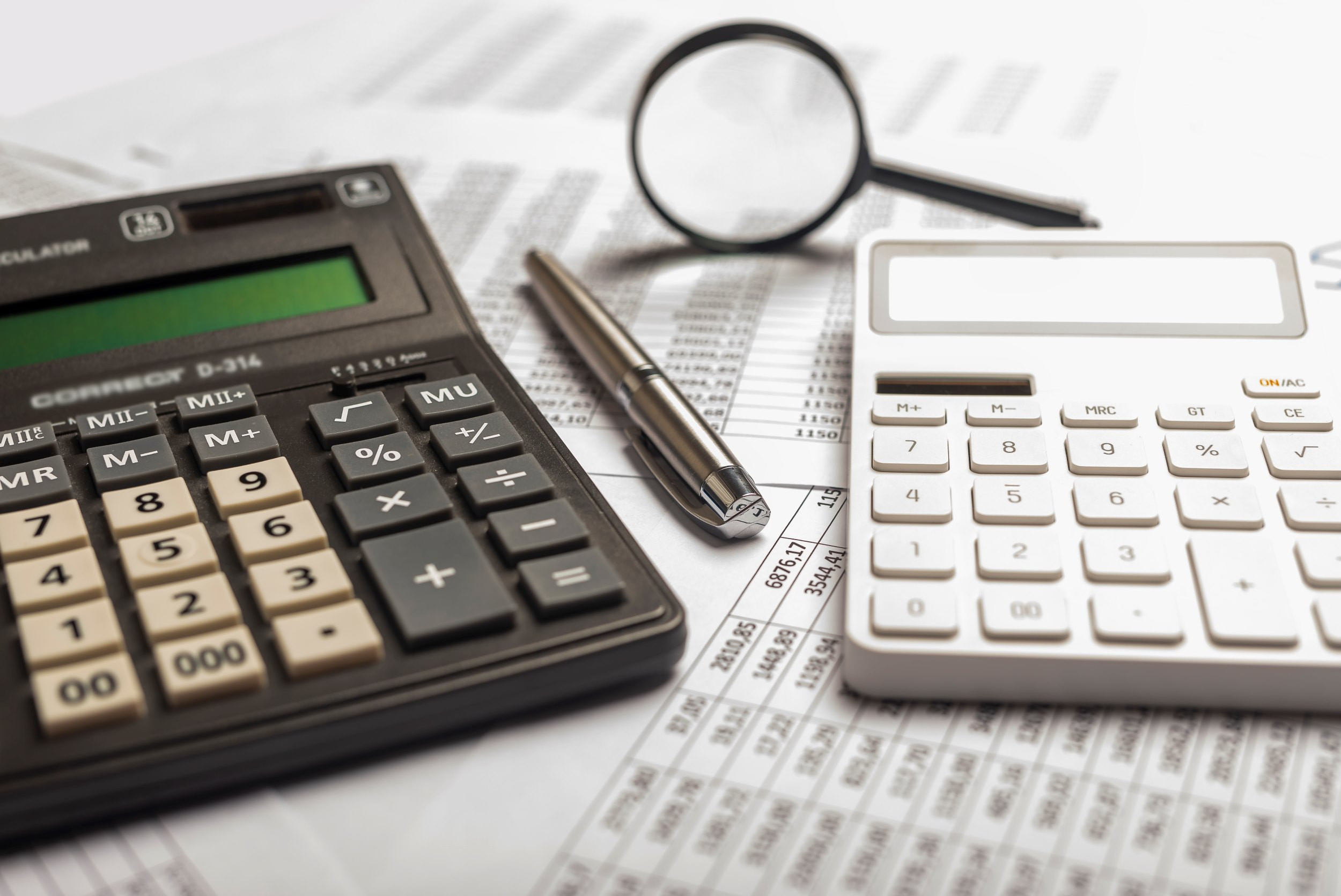 a desk with two calculators, documents and a pen