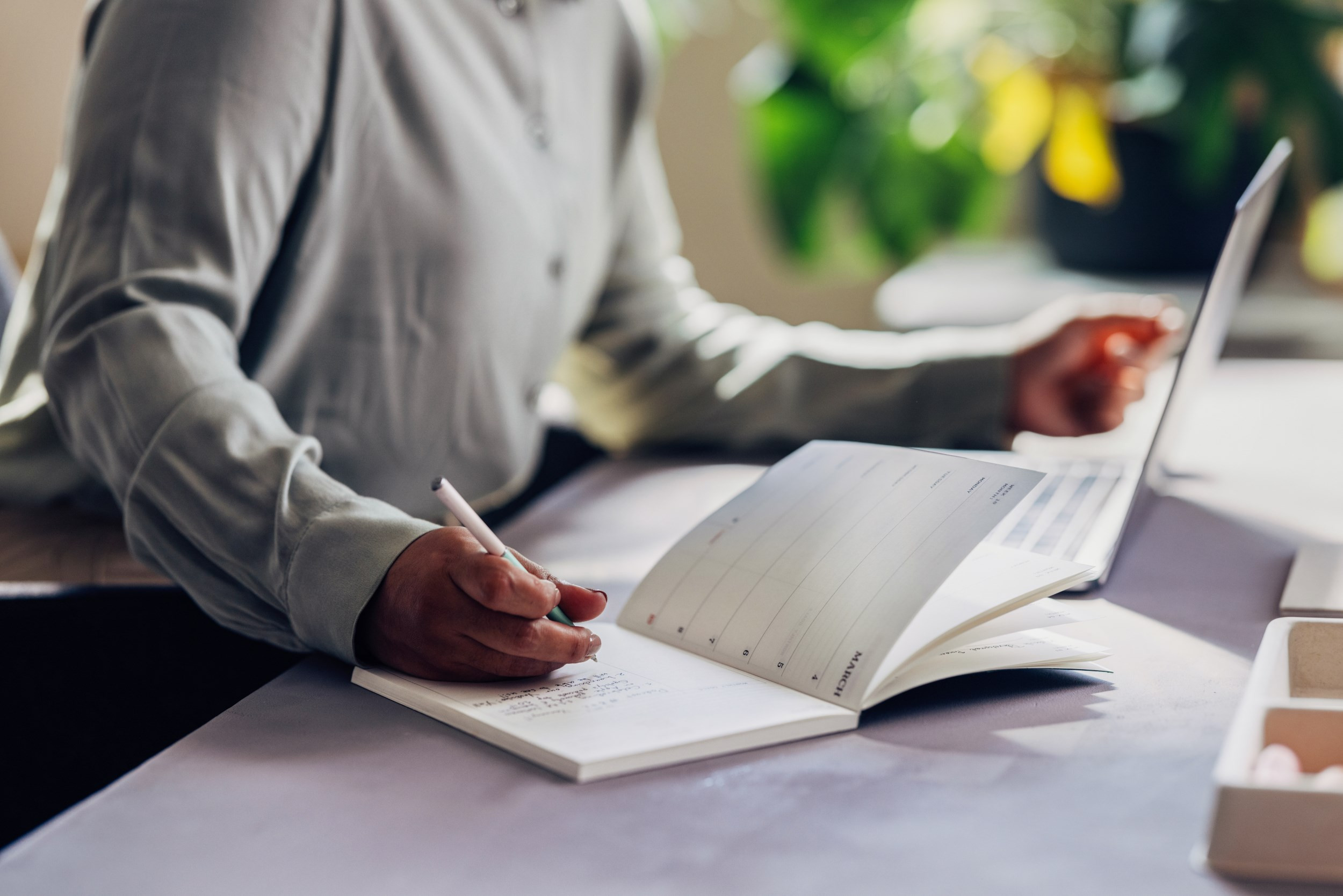 taking notes on a planner while using a laptop