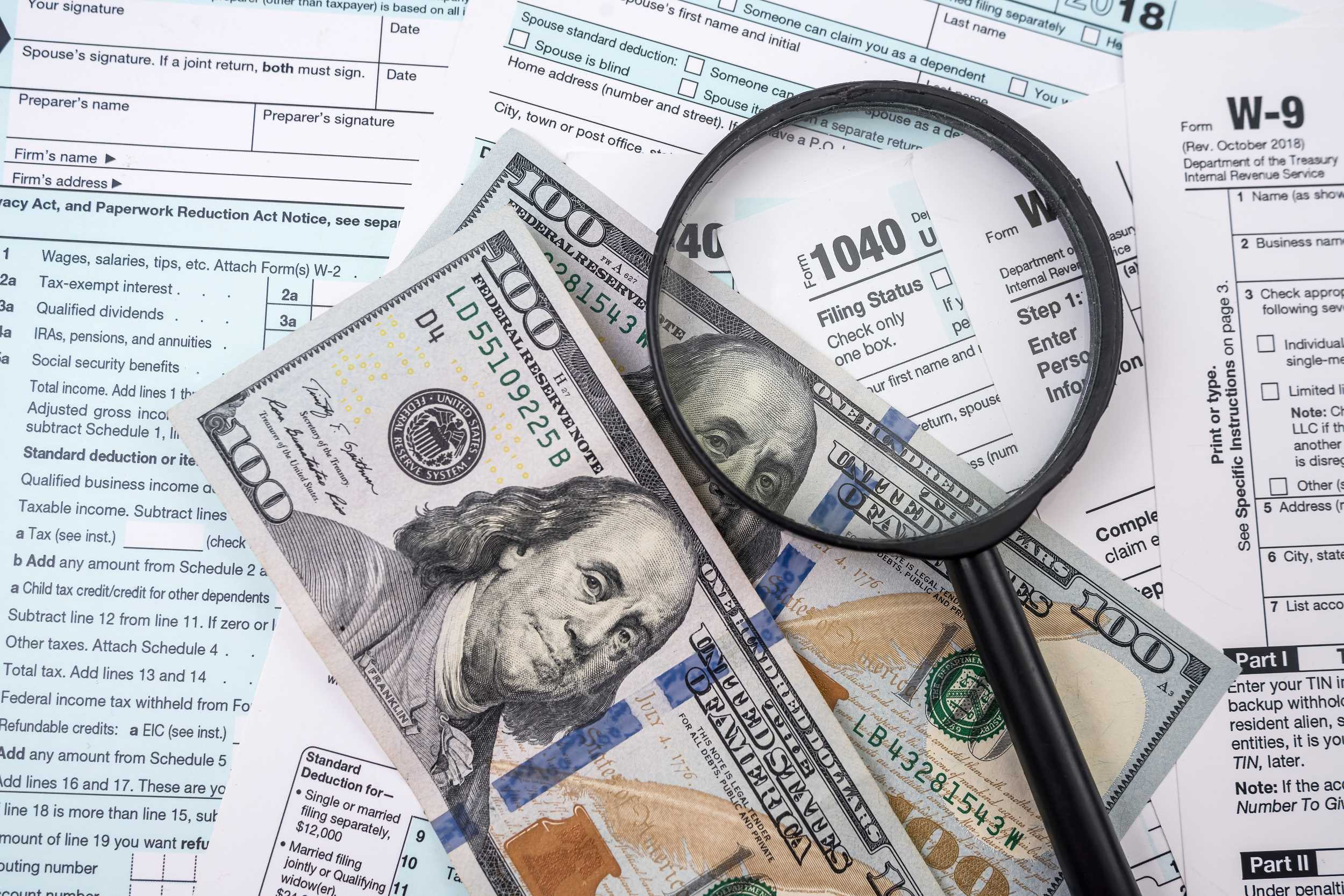 tax forms, dollar bills and a magnifying glass