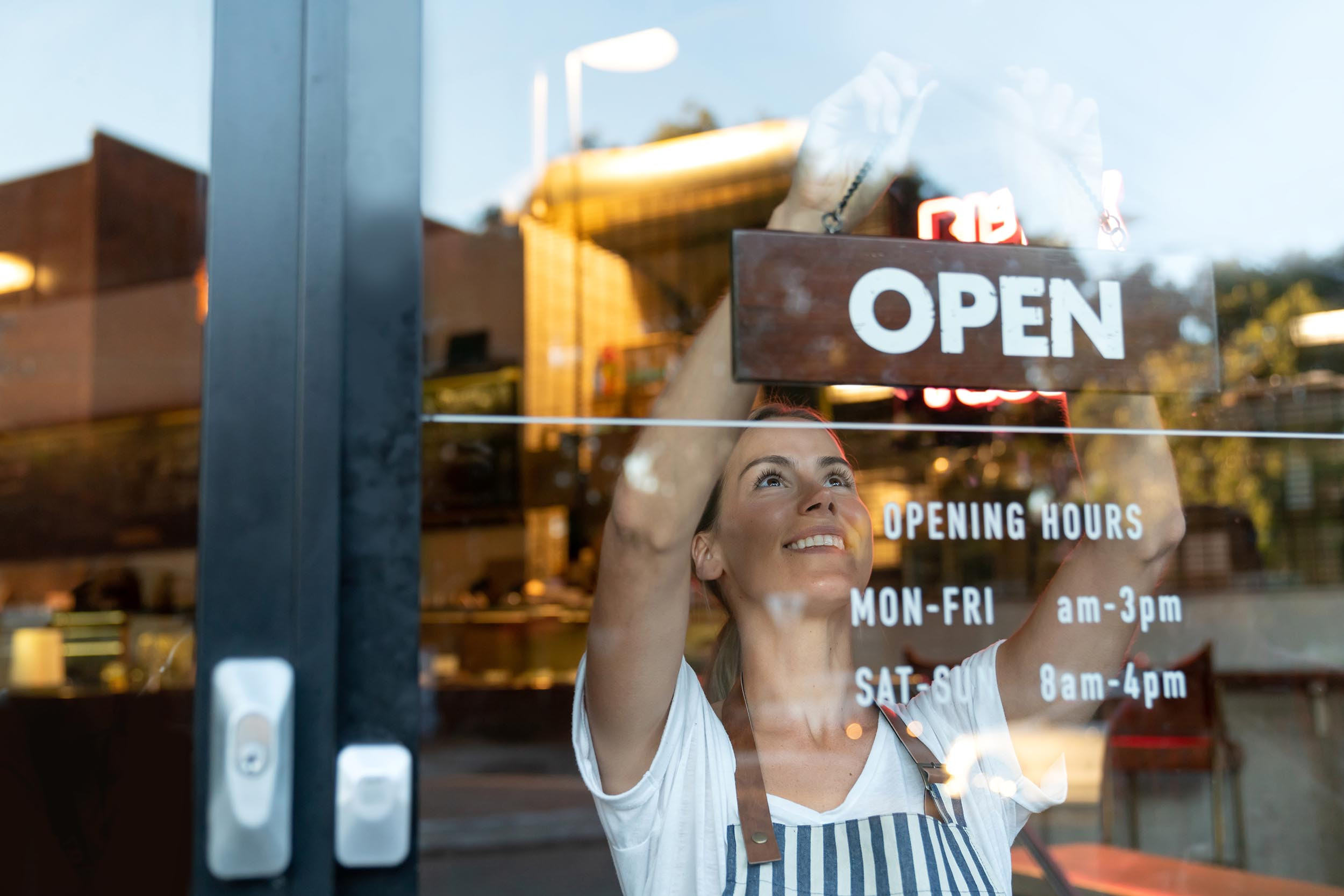a person hanging the open sign board to mention the opening hours of the shop