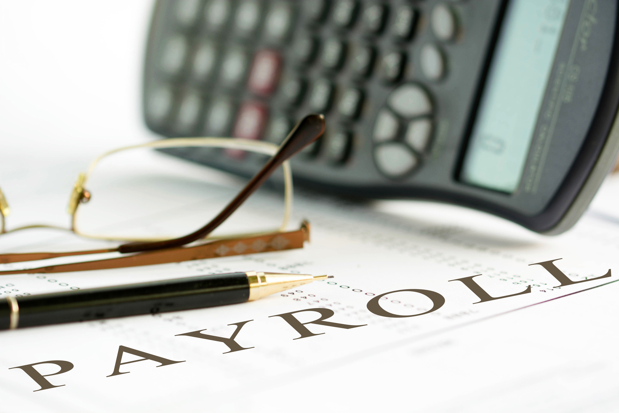 payroll paper with calculator, pen and eyeglasses