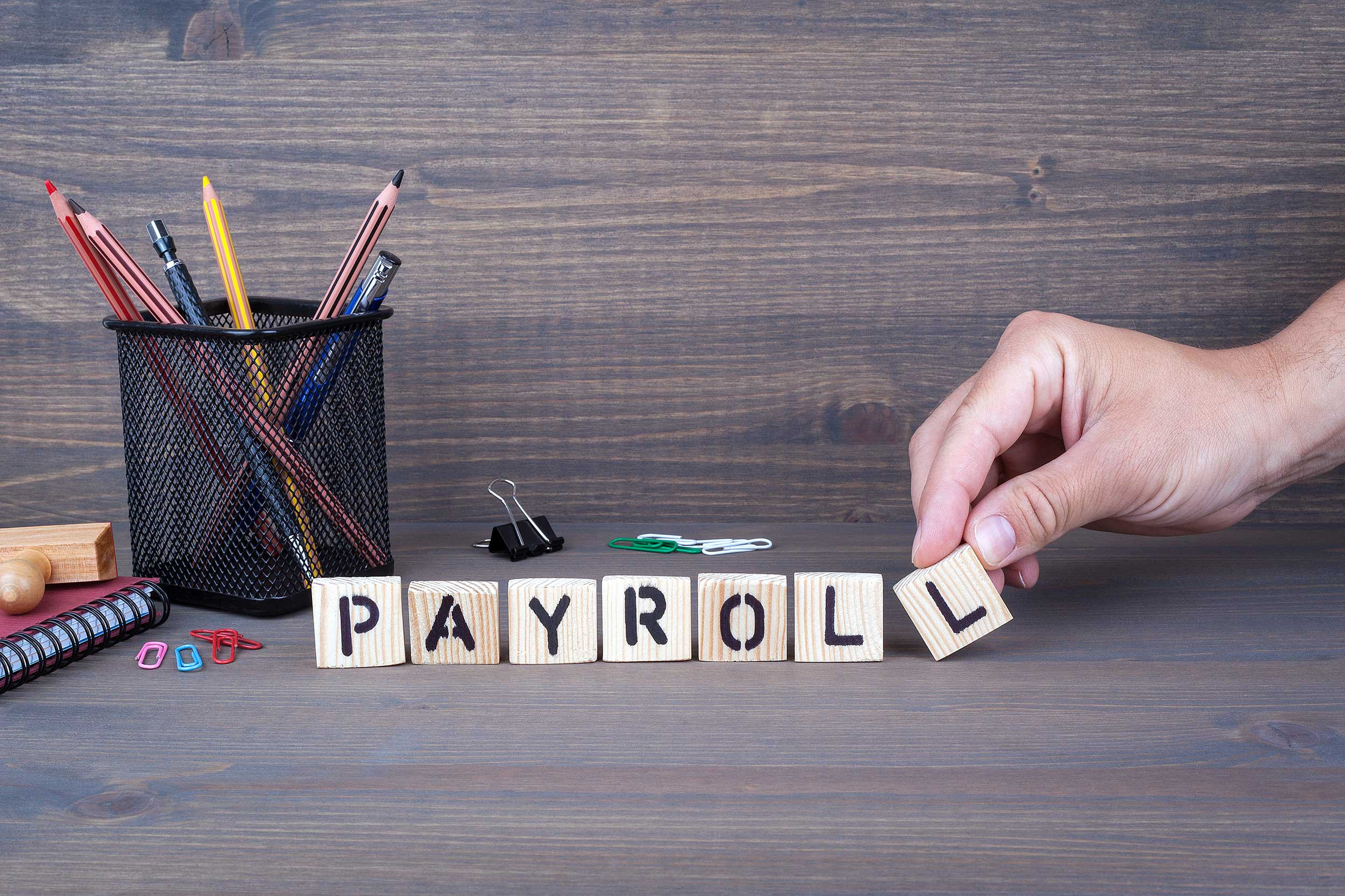 payroll word formed by wooden blocks and arranged by a hand Finger on a Table
