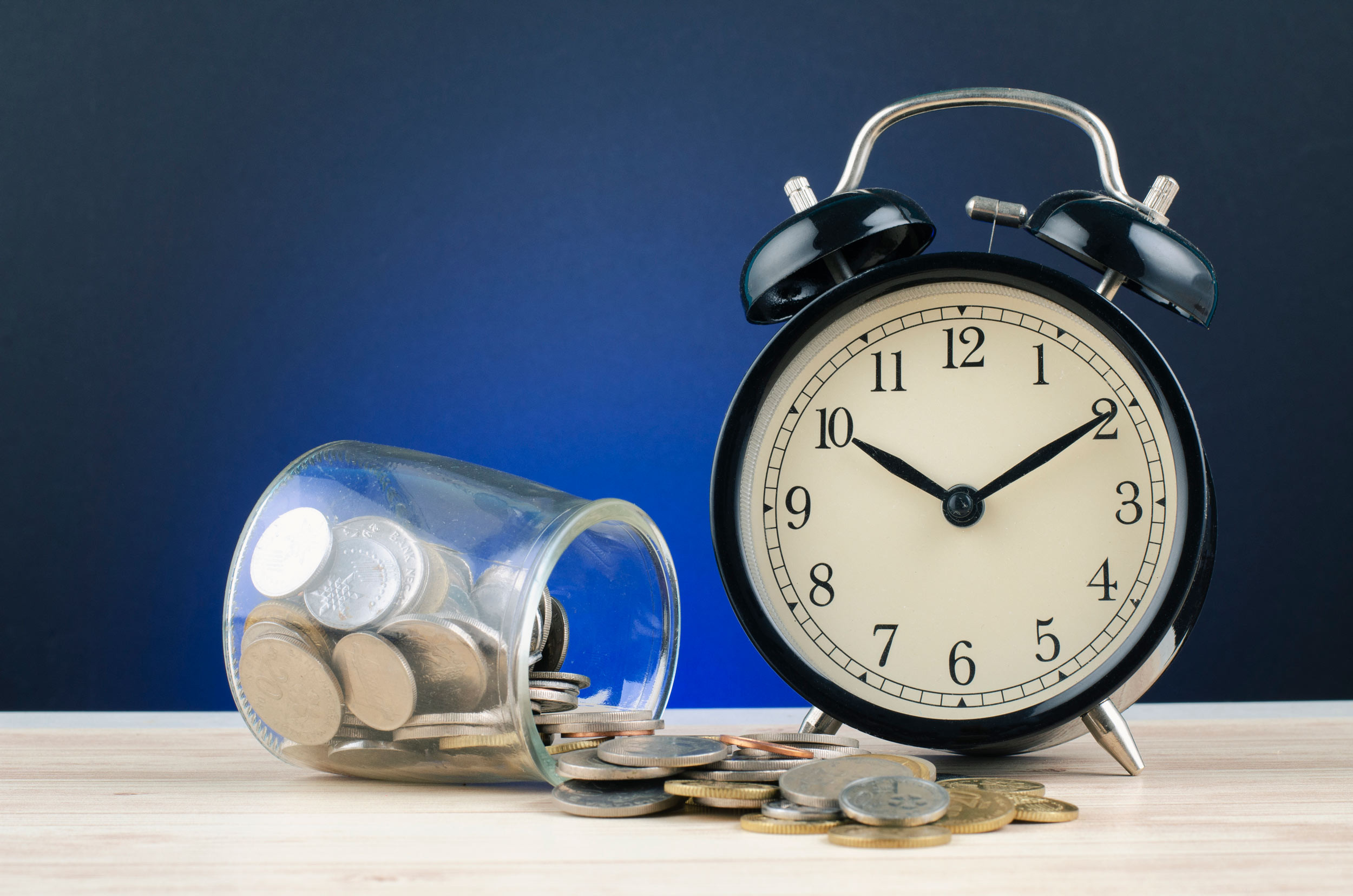 time is money concept with alarm clock and coins on table
