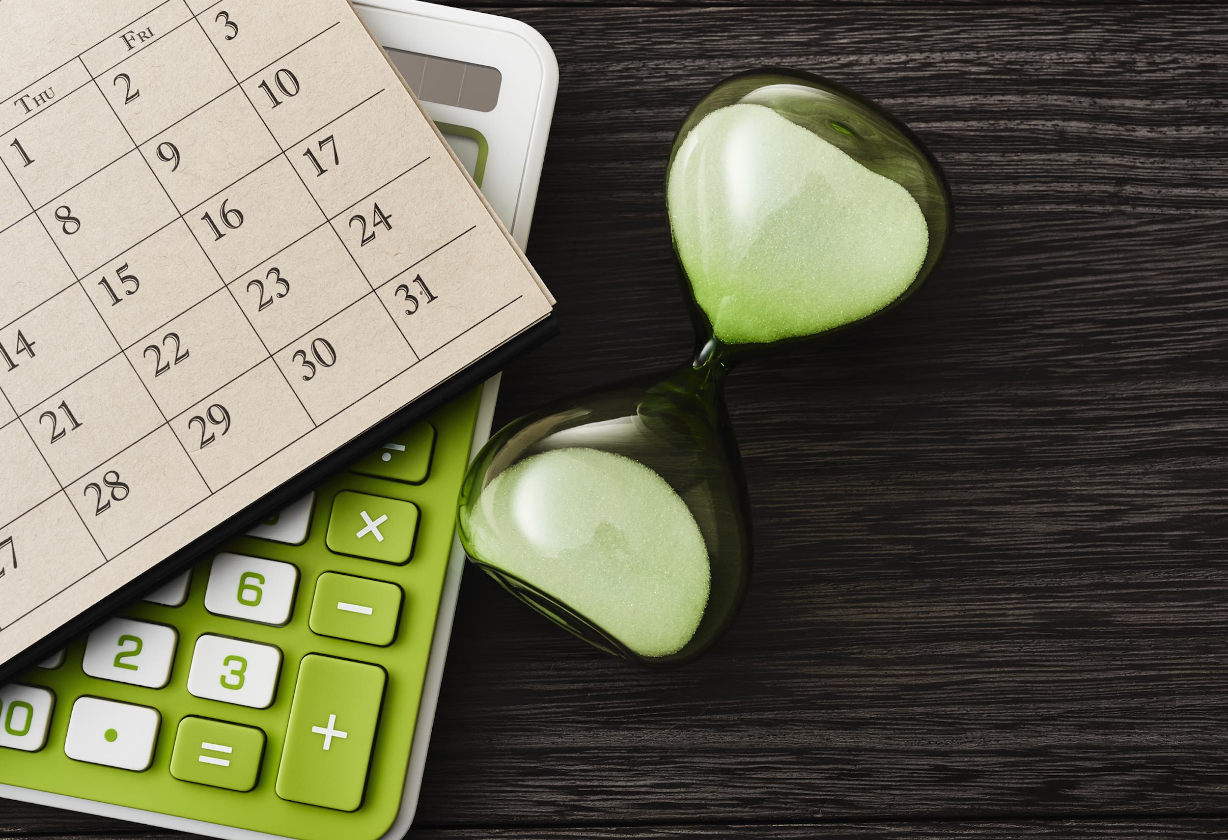 hourglass, calculator and calendar on wooden table