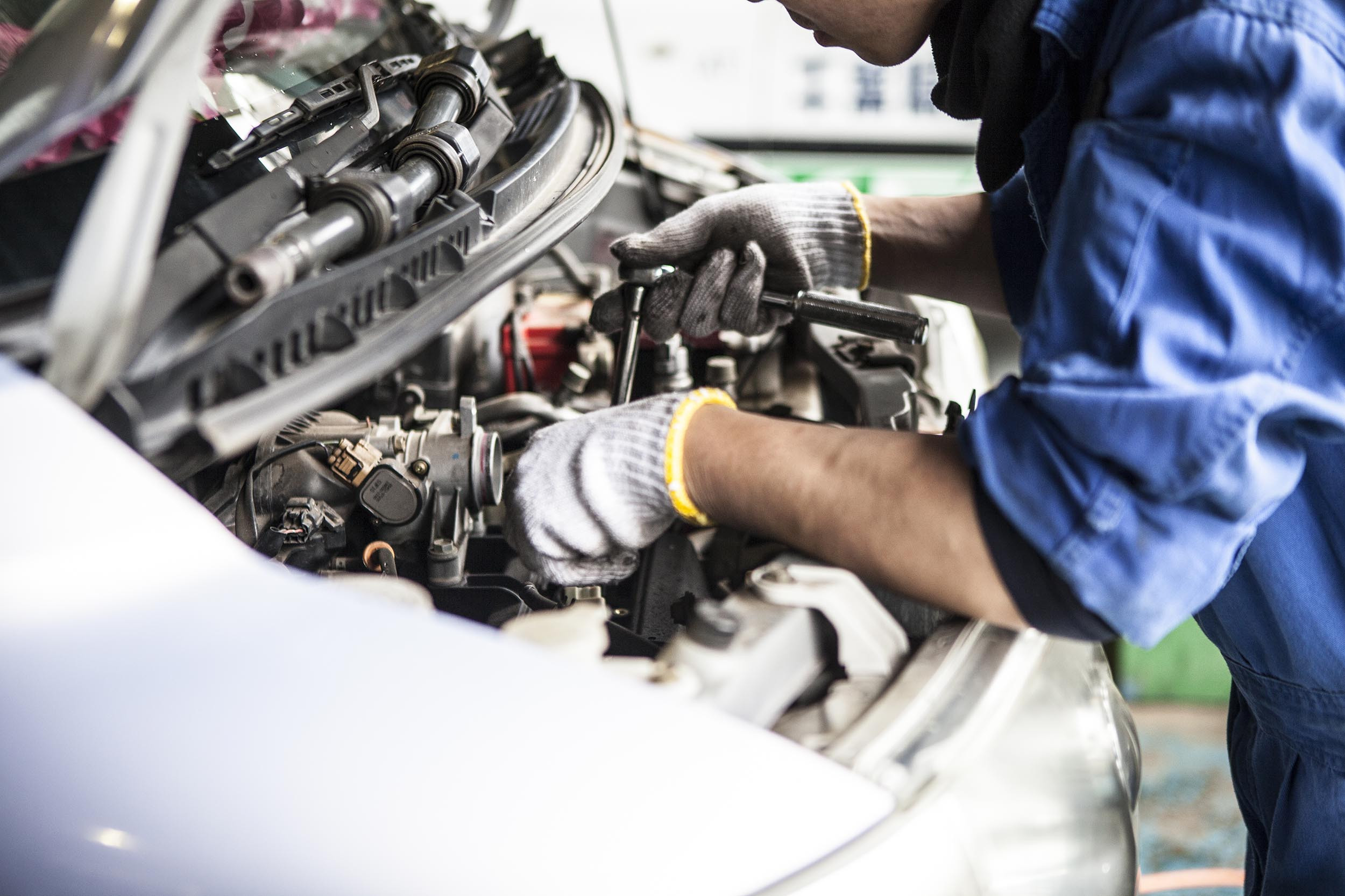 mechanic working on car engine in auto body shop