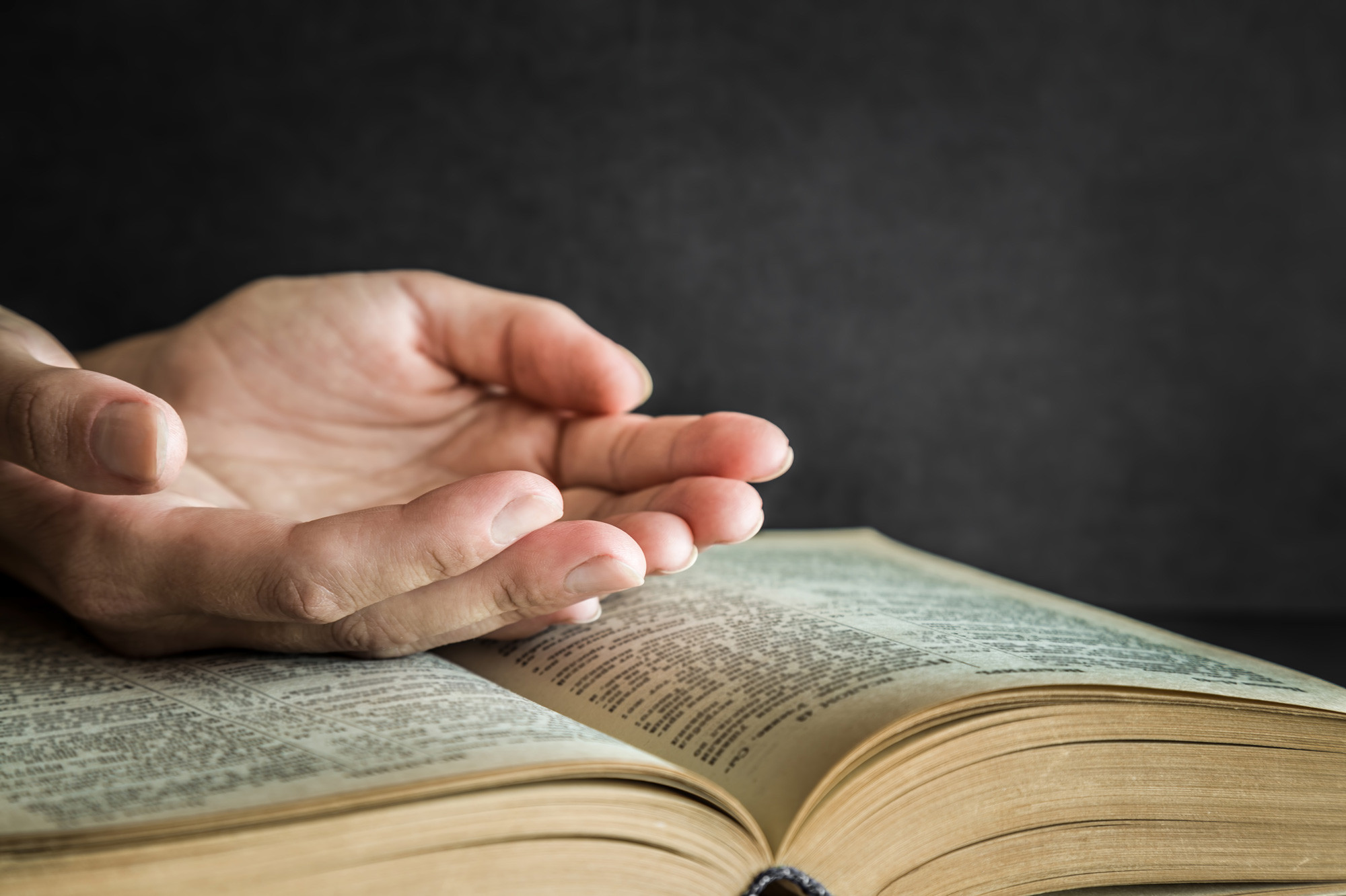 person is praying the pastor bible on dark background