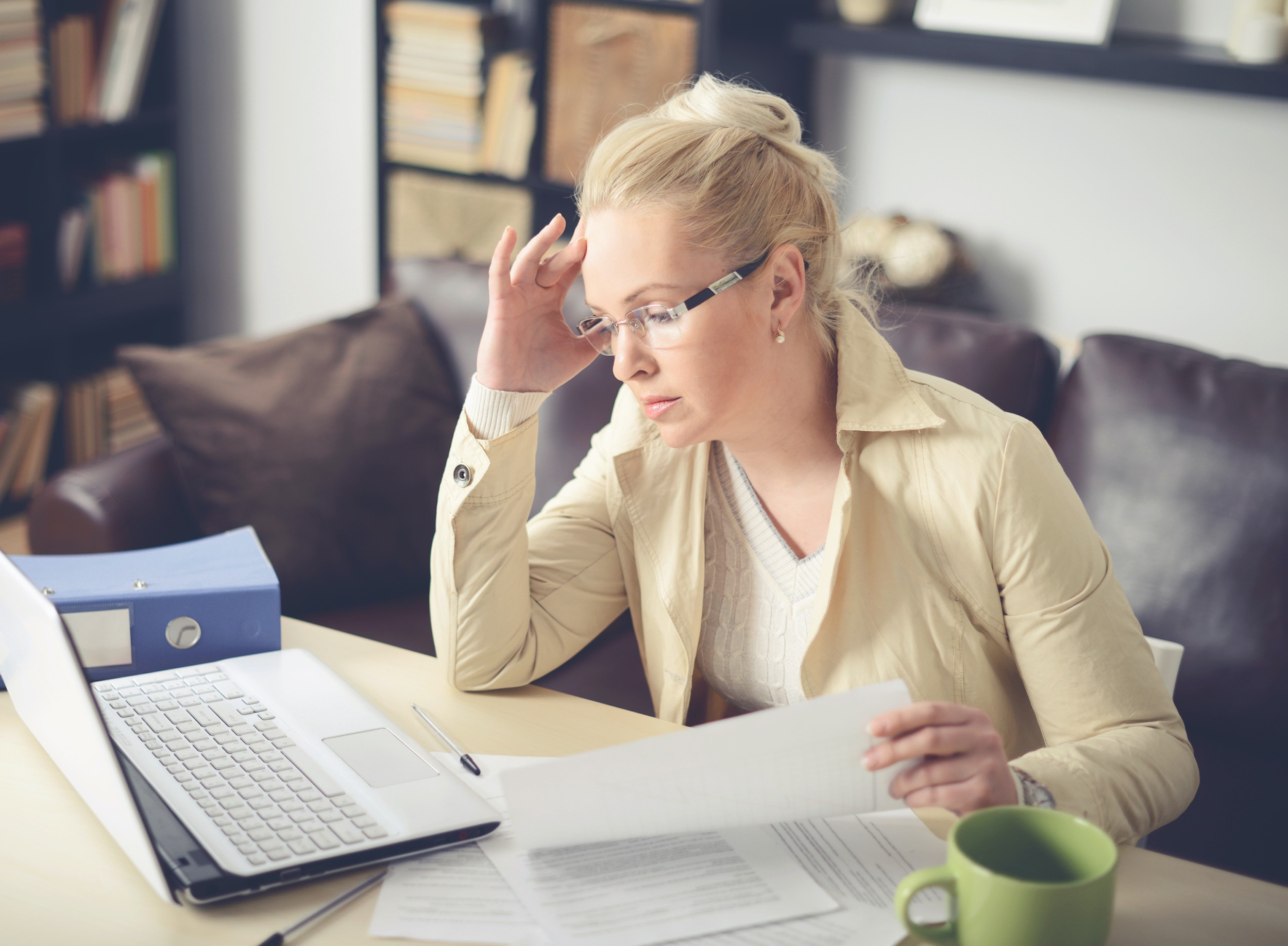 person frustrated by paperwork while using laptop at home