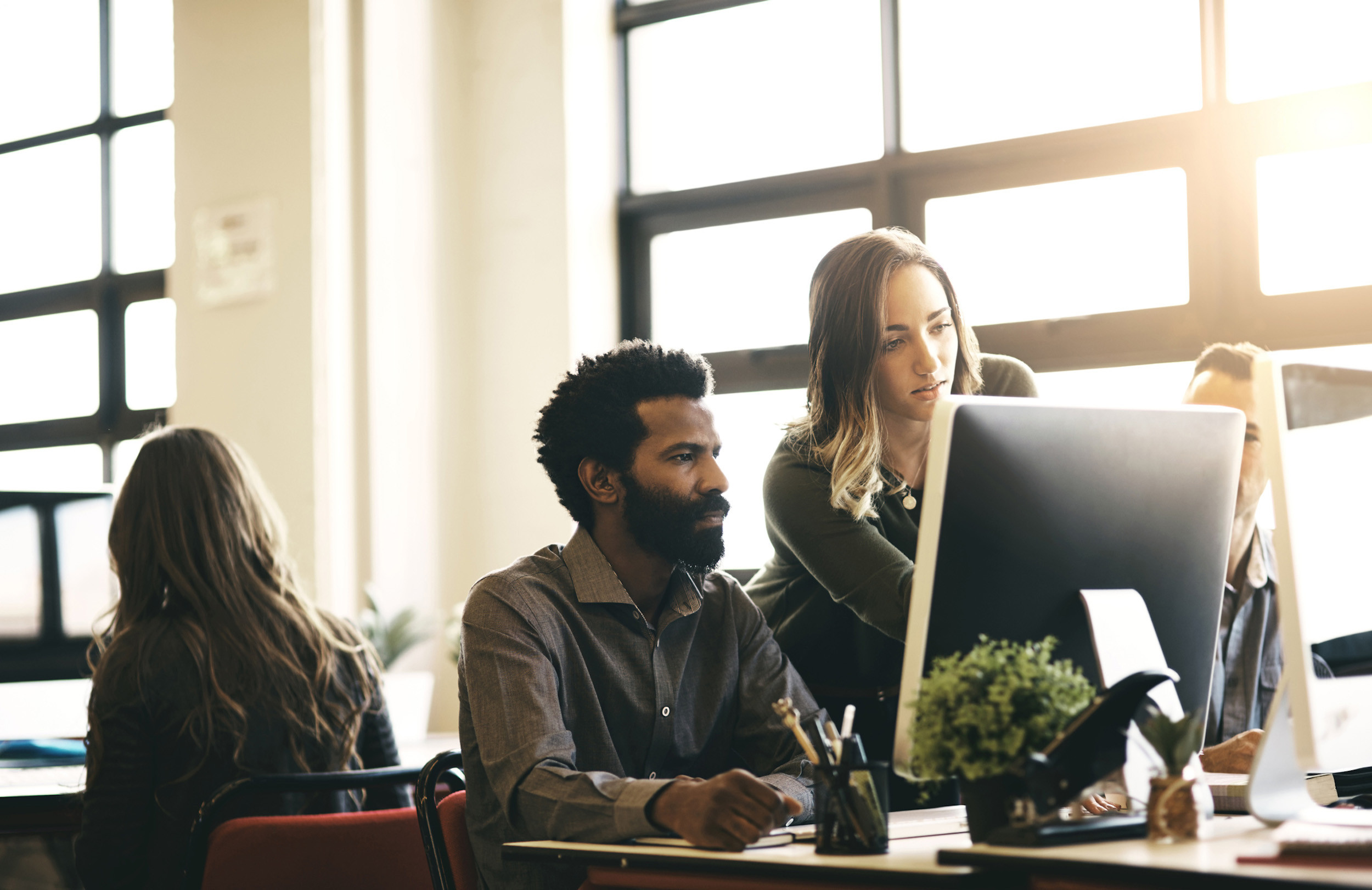 a person sitting at desk and another person helping on computer
