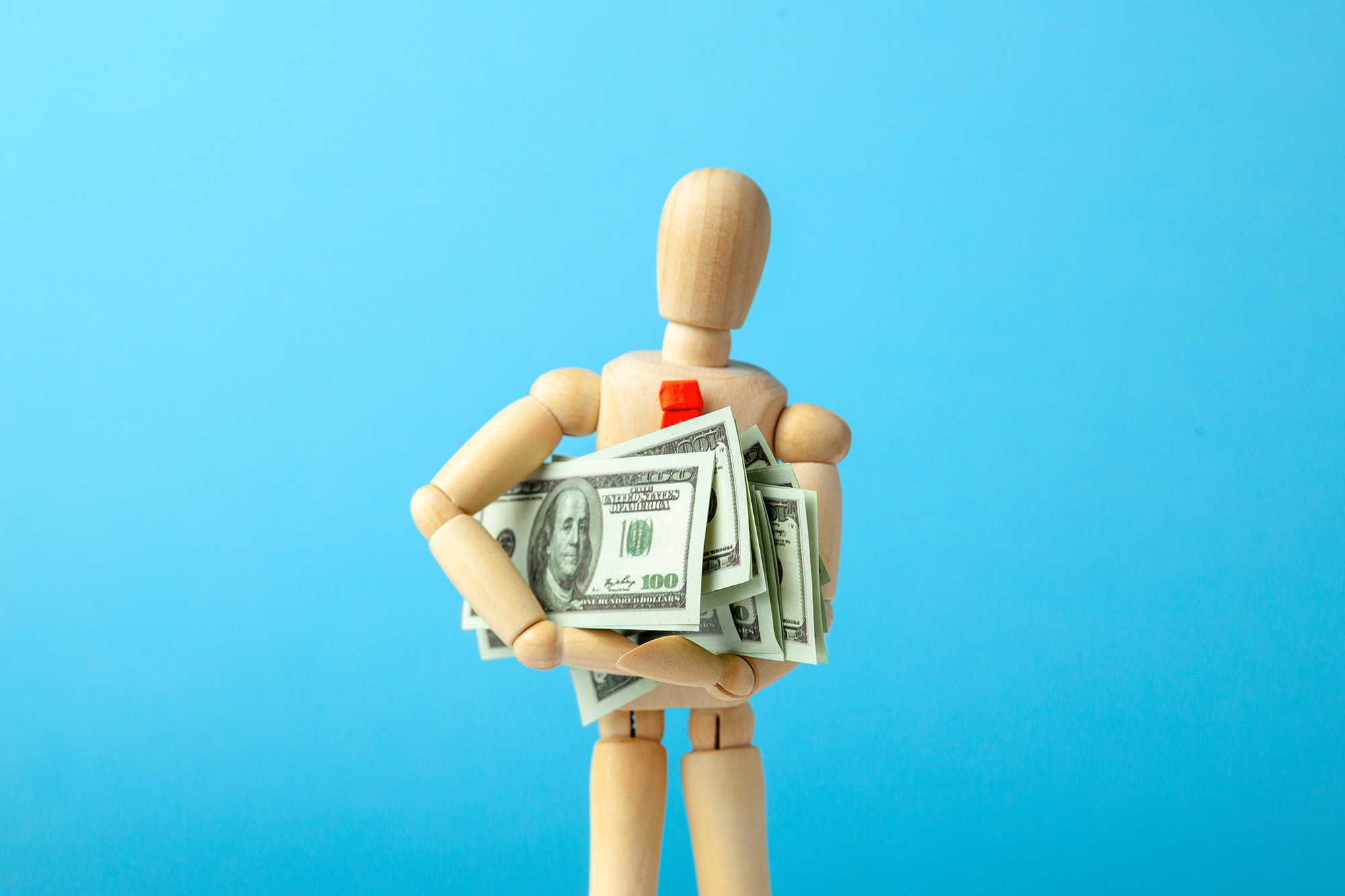 A wooden puppet holding a bunch of fake dollar bill