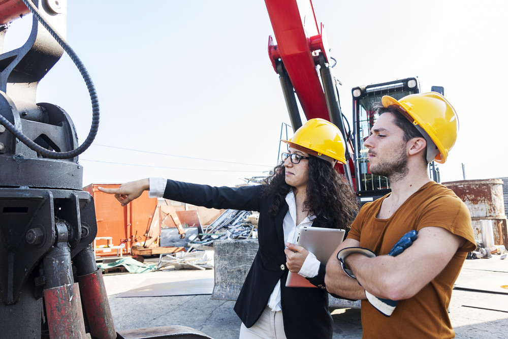 Researchers wearing construction hats analyzing equipment at a construction site.