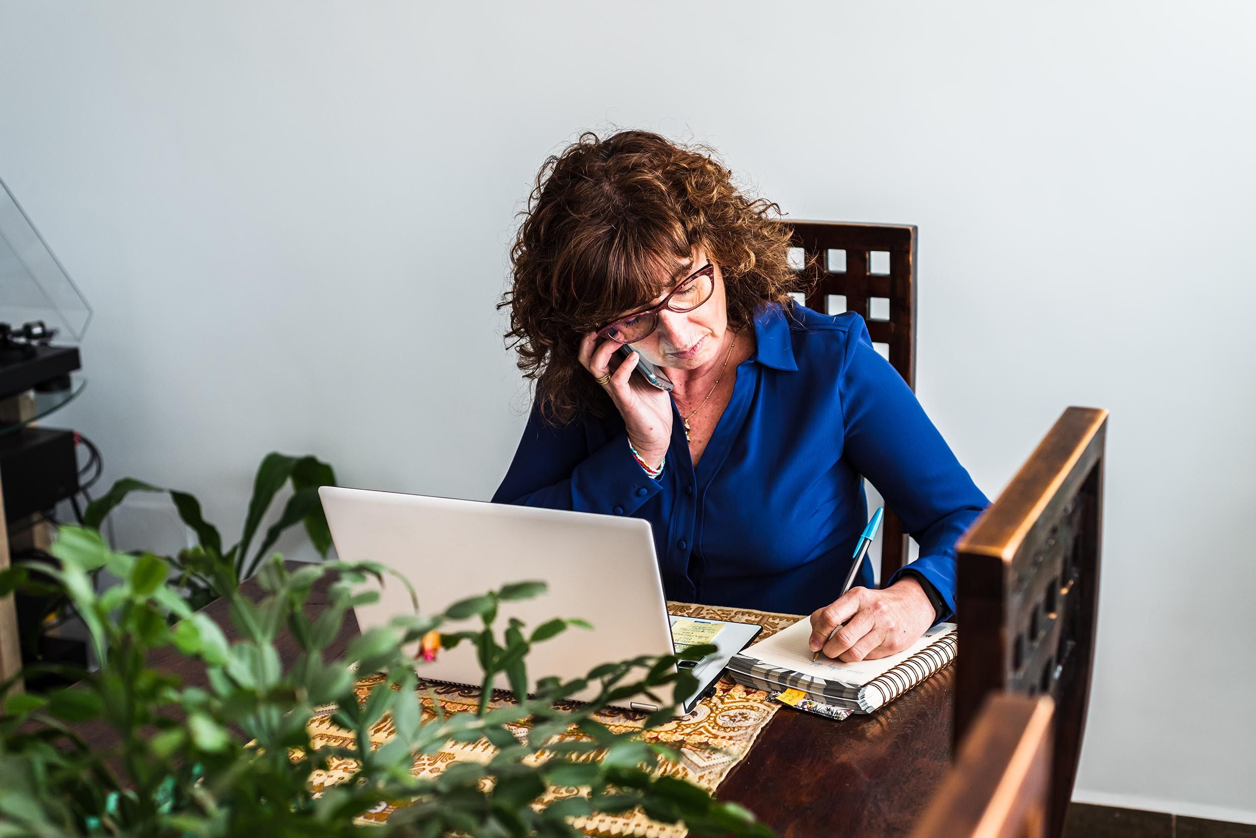 Freelance writer writing in her notebook while making a call
