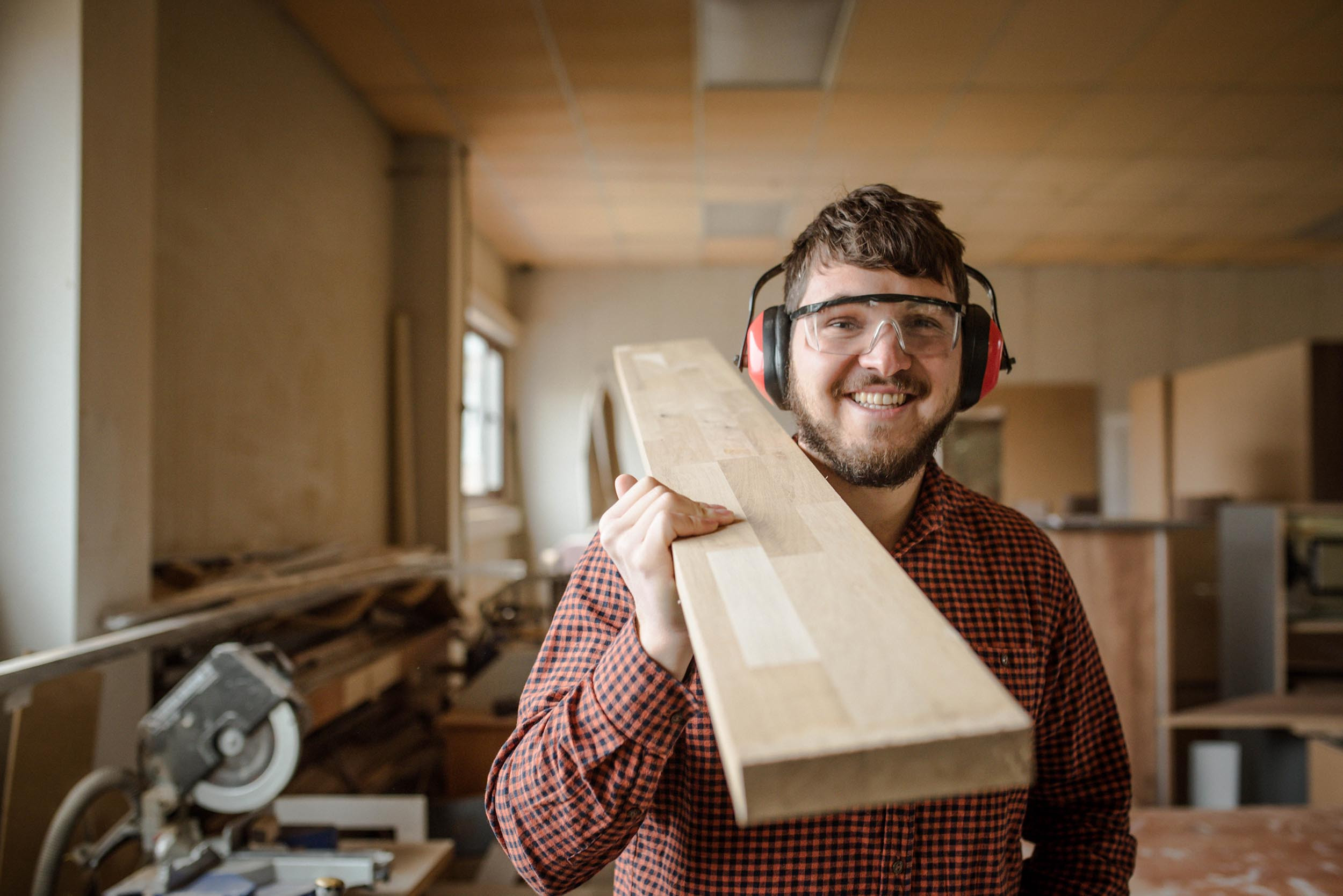 A smiling carpenter carries a beam at a residential house under construction